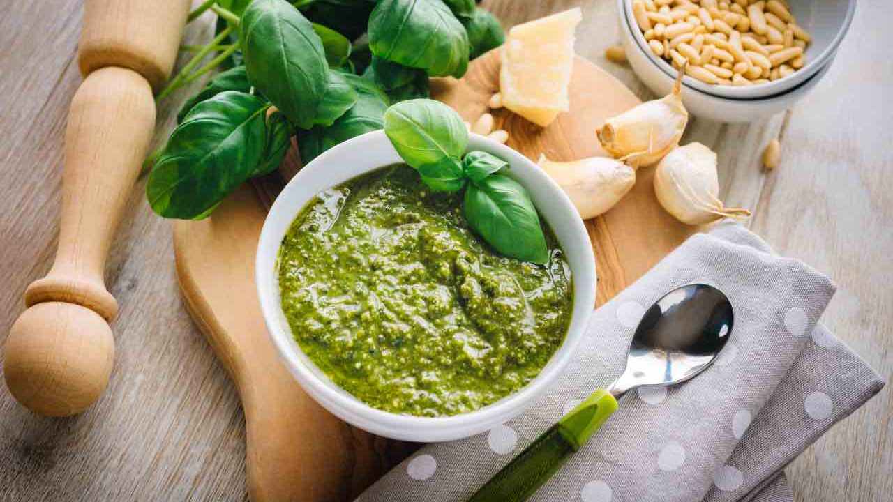 Una ciotola di pesto su un tagliere con accanto l'aglio e il basilico